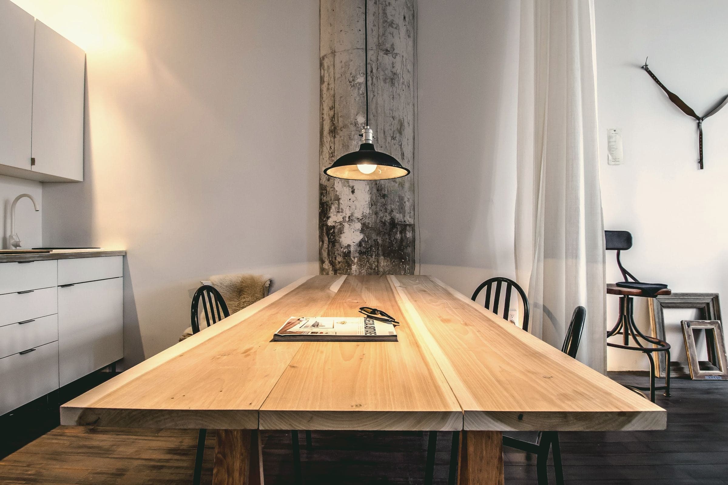 Grande table en bois massif sous une suspension, dans une pièce claire.