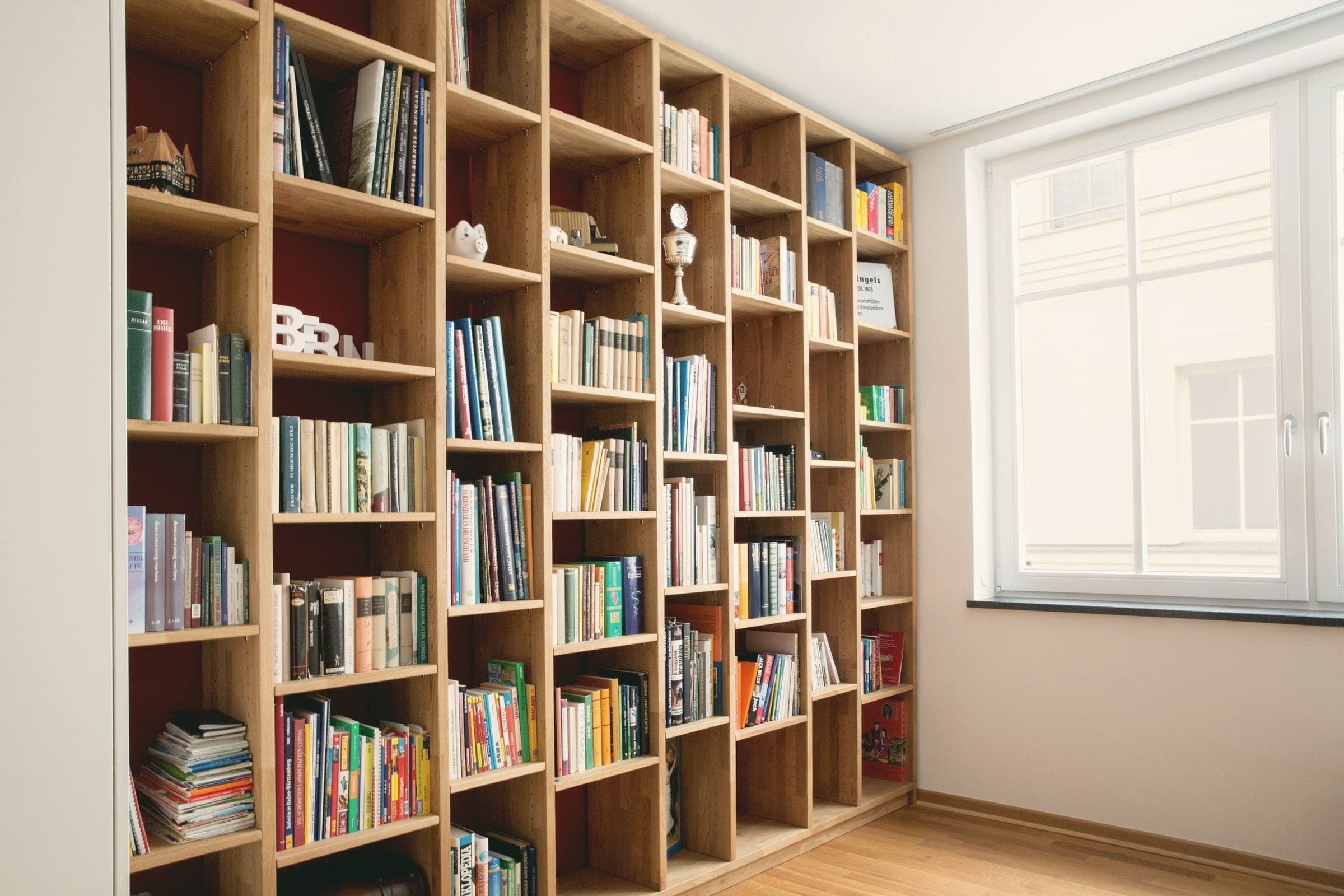 Bibliothèque en chêne à fond rouge, du sol au plafond, près d’une fenêtre.