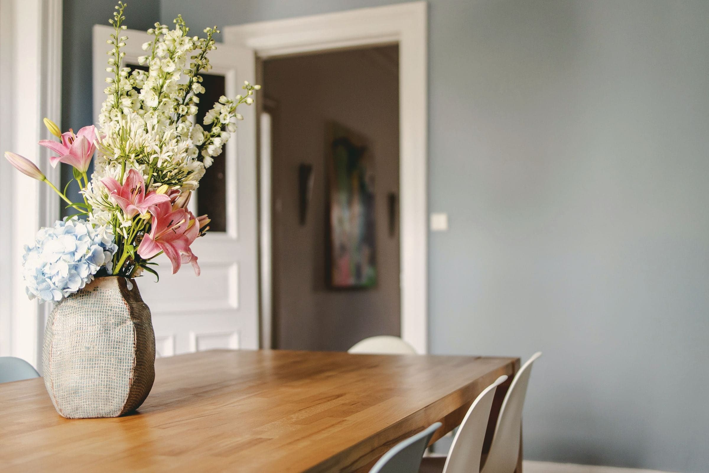 Table en chêne massif dans une salle à manger aux murs gris, bouquet posé sur le plateau.